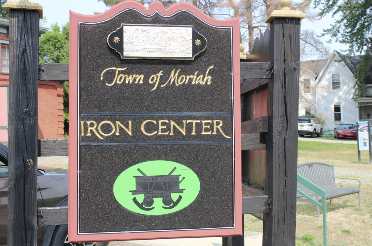 A carved and painted wood sign that reads "Town of Moriah Iron Center"